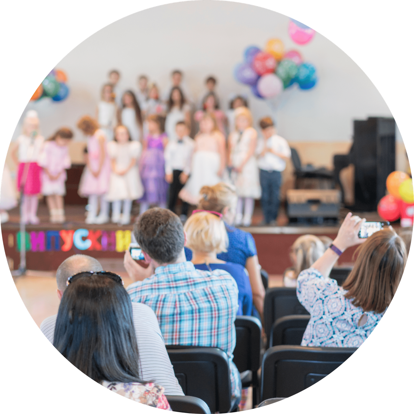 Children on stage during a school concert, parents in the audience filming them on their phones